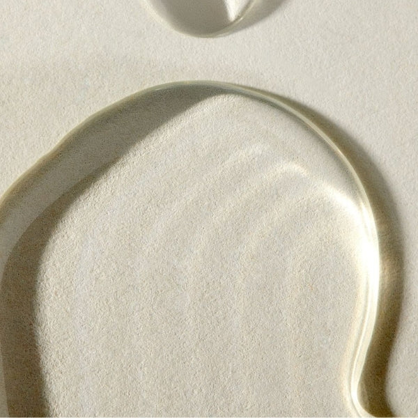 A close-up of plant derived squalane,  resting on a textured off-white surface, casting a soft shadow.